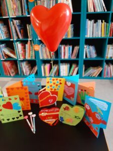 papierowe walentynkowe laurki z serduszkami na tle regału bibliotecznego z ksiązkami